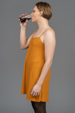 Vista lateral de una persona no binaria con un vestido tomando una copa