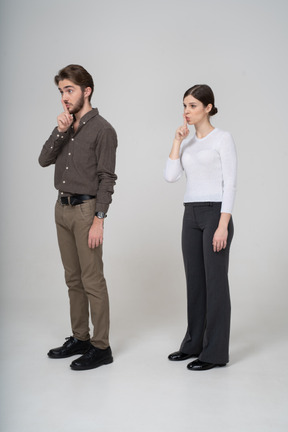 Three-quarter view of a young couple in office clothing showing silence gesture