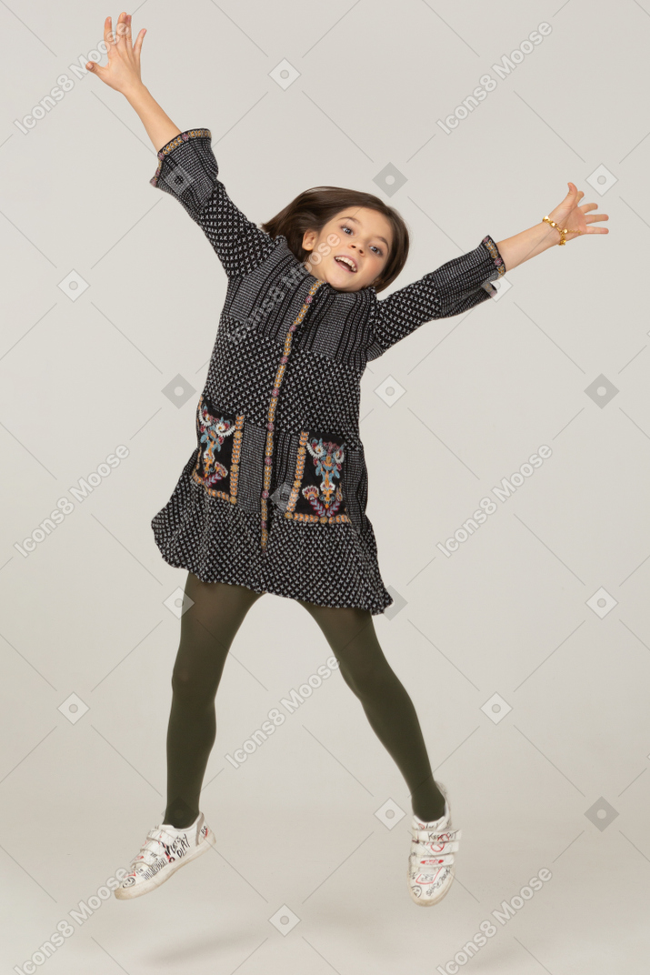 一个跳跃的小女孩的前视图，她穿着伸展手和腿的裙子