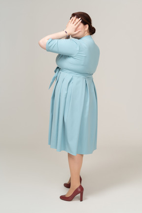 Vista lateral de uma mulher de vestido azul fechando os olhos com as mãos