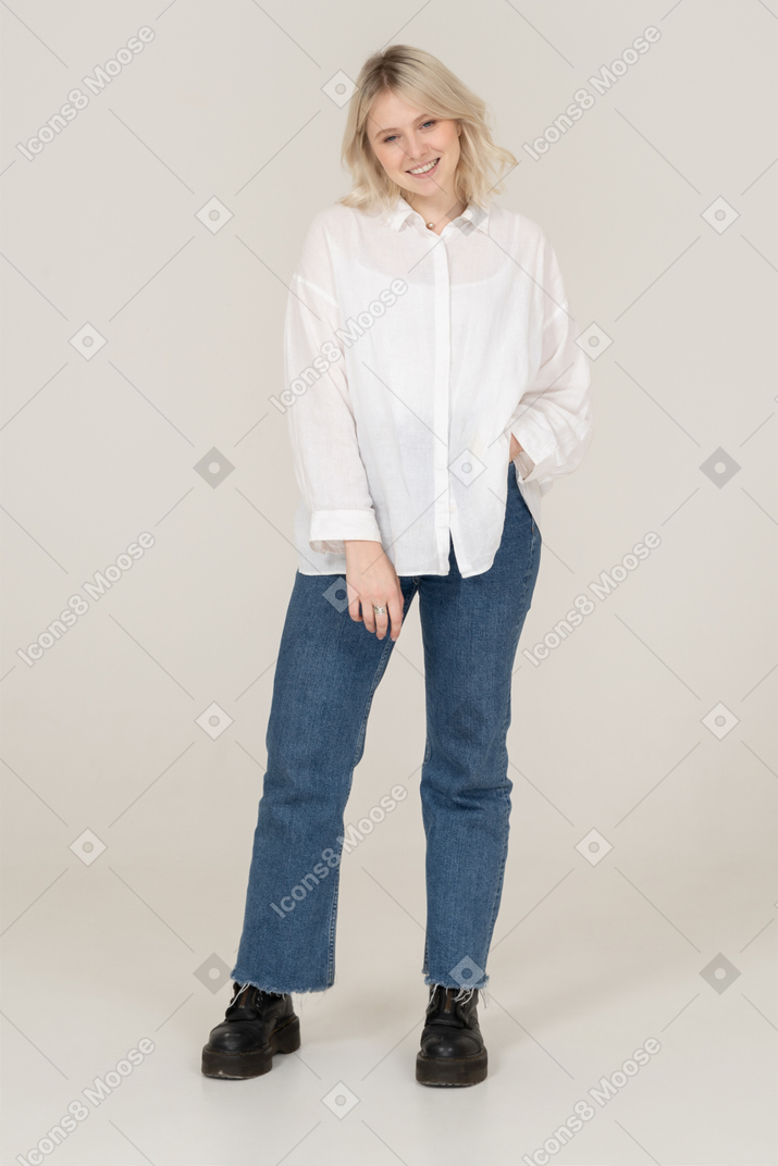 Front view of a young smiling female in casual clothes putting hands in pocket and looking at camera