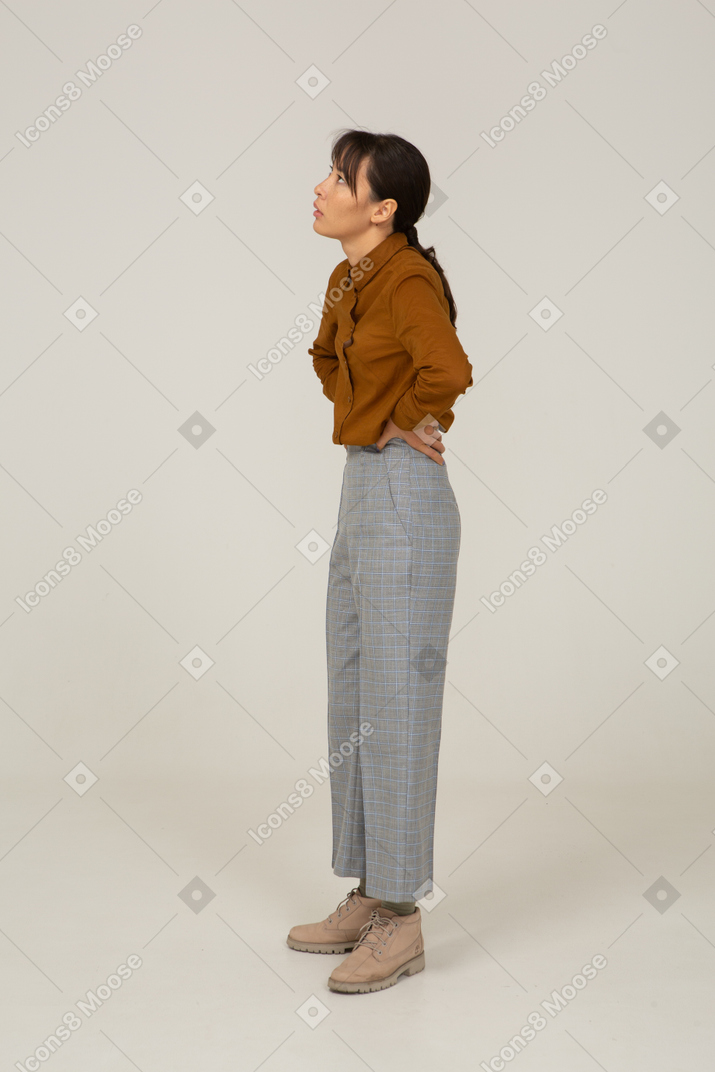 Vista di tre quarti di una giovane donna asiatica in calzoni e camicetta che mette le mani sui fianchi