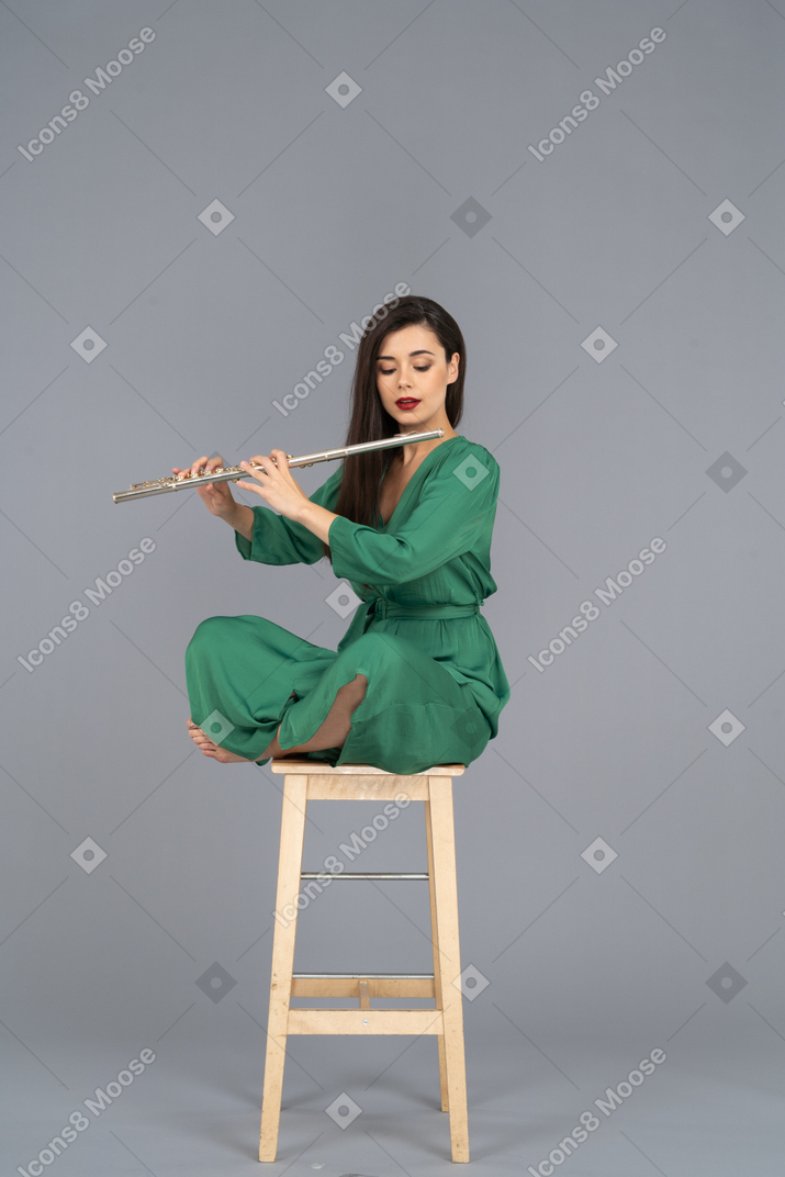 In voller länge einer jungen dame, die die klarinette betrachtet, die mit gekreuzten beinen auf einem holzstuhl sitzt
