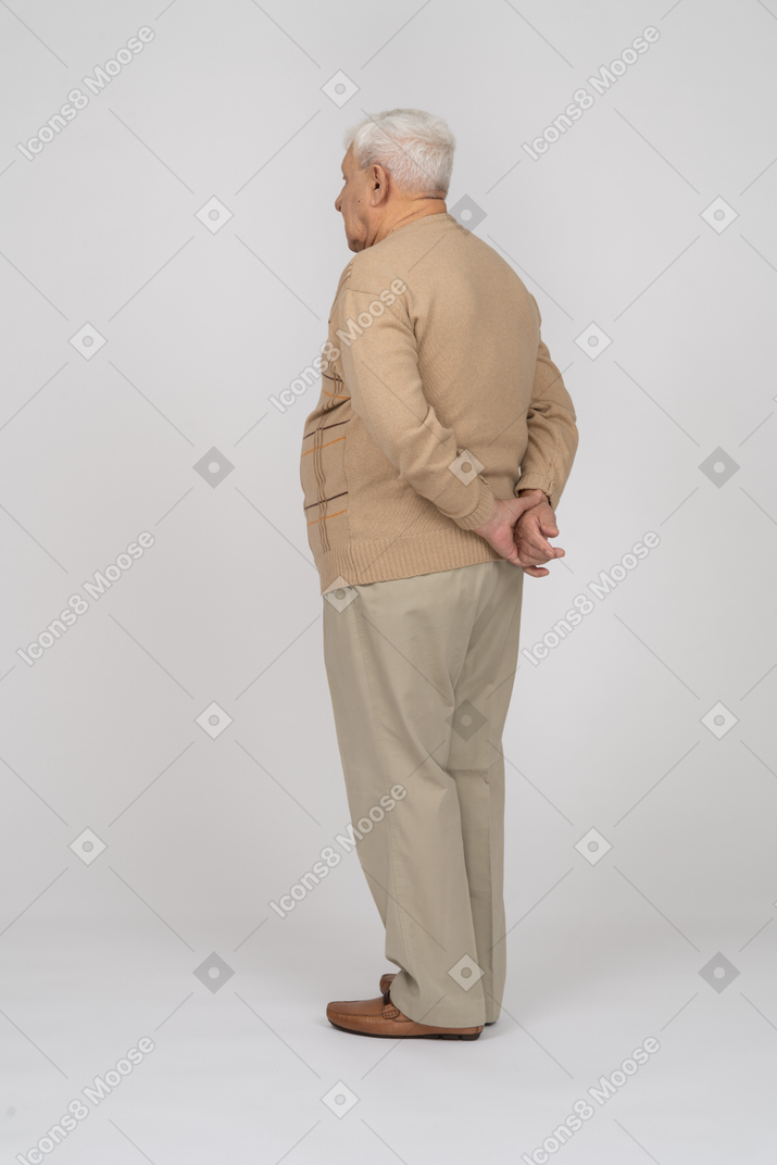 Vue latérale d'un vieil homme en vêtements décontractés posant avec les mains derrière le dos