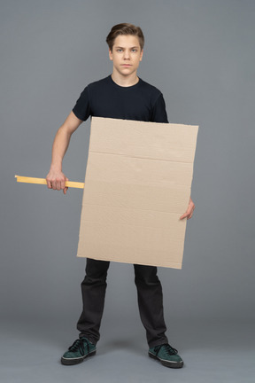 Joven serio de pie con un cartel en blanco