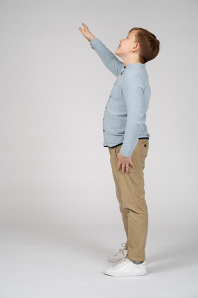 Vista lateral de um menino alegre olhando para cima e acenando