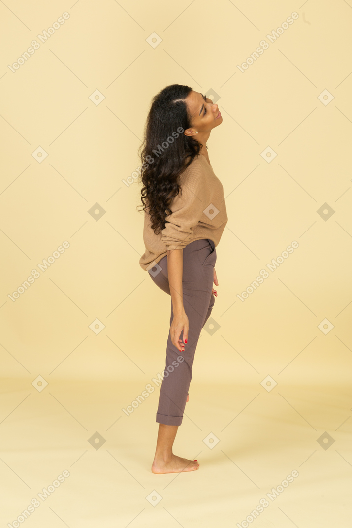 Vista posterior de tres cuartos de una mujer joven de piel oscura reclinada hacia atrás