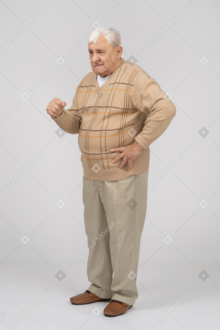 Vista laterale di un vecchio in abiti casual in piedi con la mano sull'anca e spiegando qualcosa