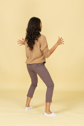 Vista posterior de tres cuartos de una divertida joven de piel oscura extendiendo sus manos y piernas