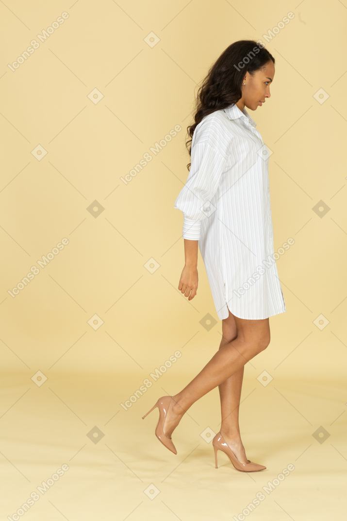 하얀 드레스를 입고 걷는 어두운 피부 젊은 여성의 측면보기