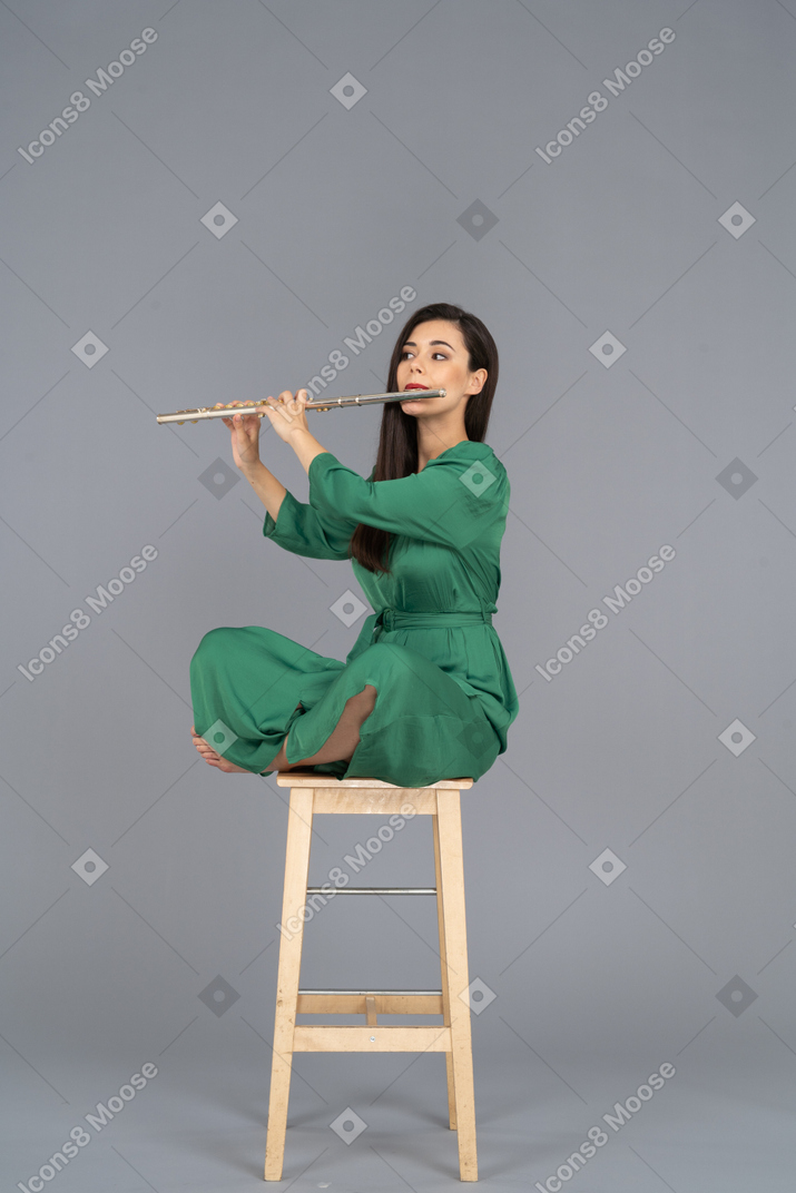 De cuerpo entero de una señorita tocando el clarinete sentada con las piernas cruzadas en una silla de madera