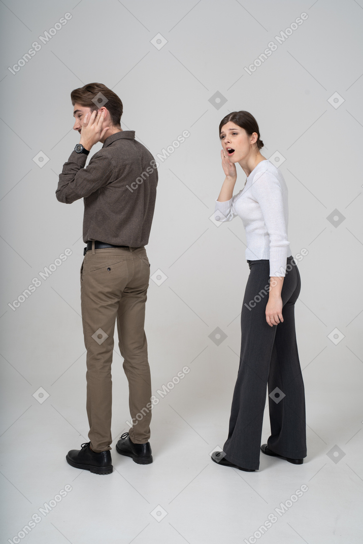 Three-quarter back view of a young couple in office clothing listening to the rumors