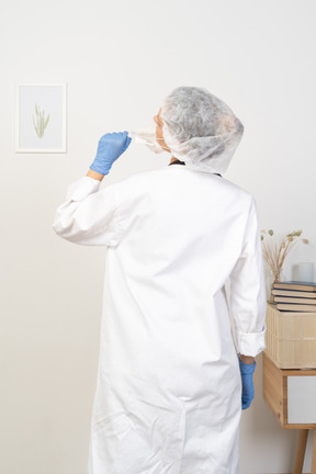 Back view of a young female doctor trying to take mask off