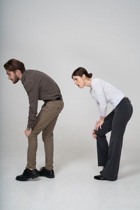 Vue latérale d'un jeune couple en vêtements de bureau touchant le genou