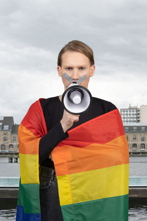 A woman with pride flag holding a megaphone in front of her face