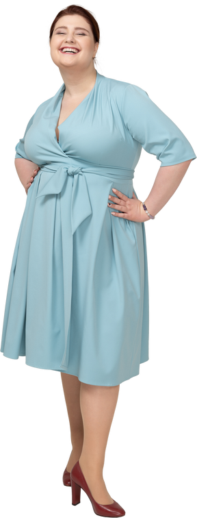 Vista frontal de uma mulher feliz em um vestido azul em pé com as mãos nos quadris