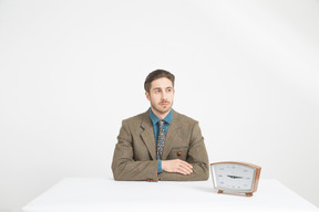 Handsome young man sitting near the clock with his hands folded