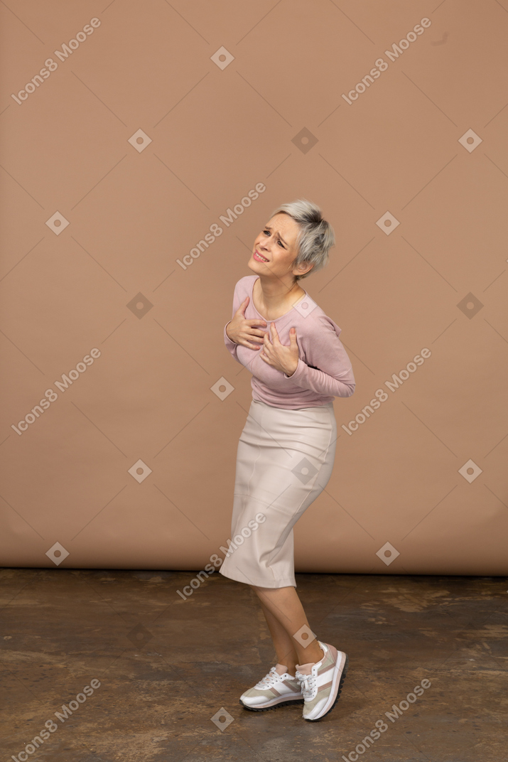 Vue latérale d'une femme émotive dans des vêtements décontractés debout avec les mains sur la poitrine