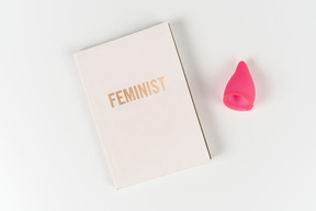 Feministisches buch und menstruationstasse auf weißem hintergrund