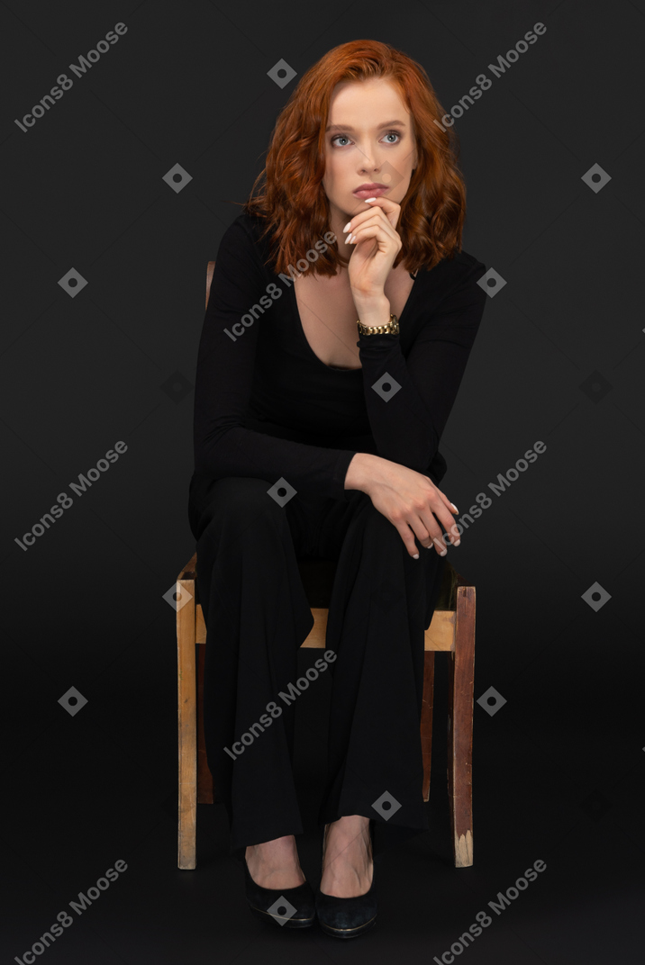 Young thoughtful woman sitting on the woden chair and touching her chin
