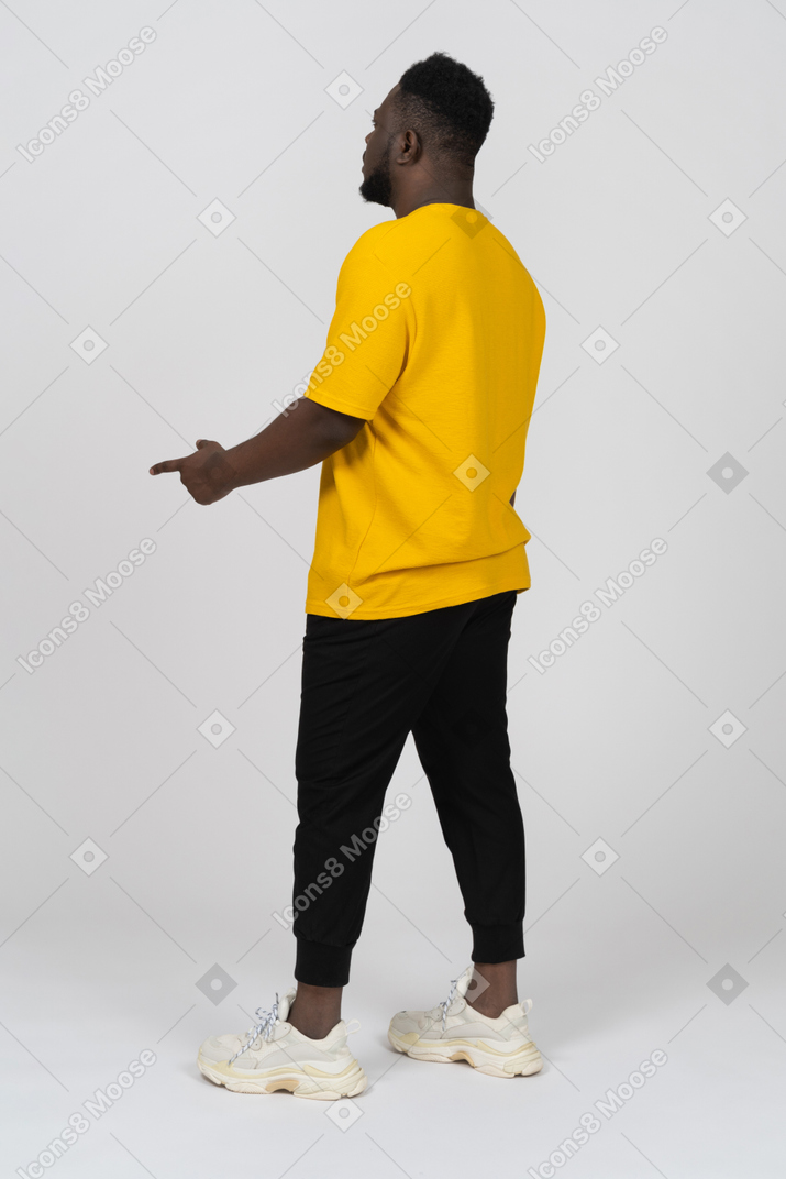 Three-quarter back view of a young dark-skinned man in yellow t-shirt pointing finger