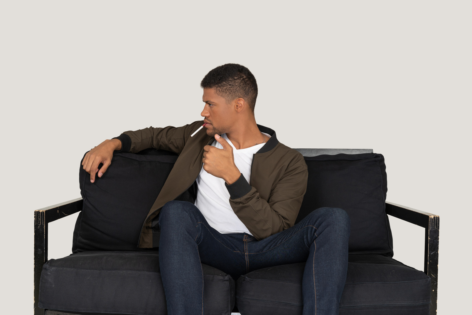 Front view of a young arrogant man sitting on a sofa and holding cigarette in mouth