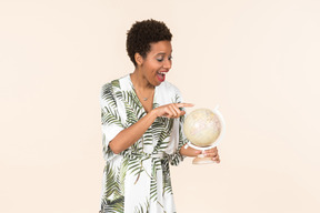 Black short-haired woman in a white and green dress, standing with a globe in her hand