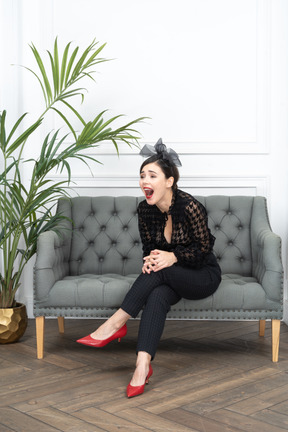 Woman sitting on couch next to a potted plant and laughing