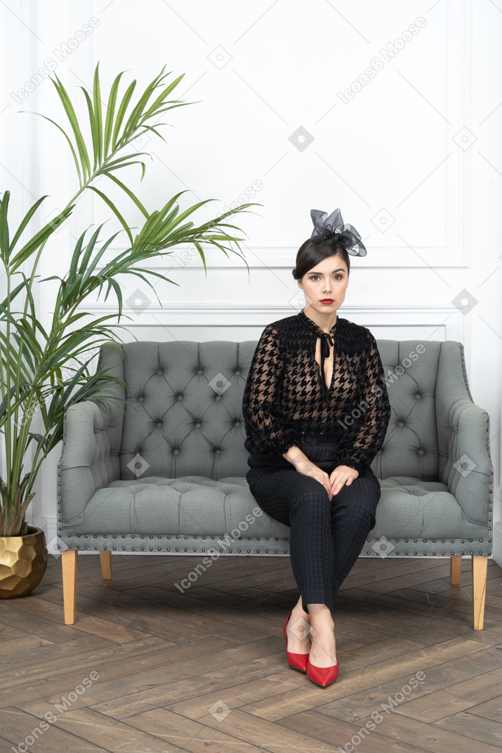 Serious woman sitting on couch next to a potted plant