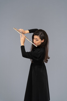 Three-quarter view of a serious young lady in black dress playing the flute