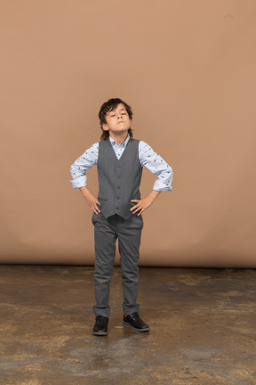 一个穿着灰色西装的男孩双手叉腰摆姿势的正面图