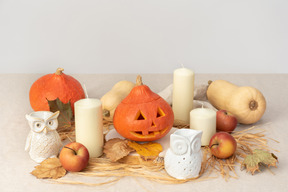 Calabazas talladas, figuras de búhos, velas y manzanas rojas.