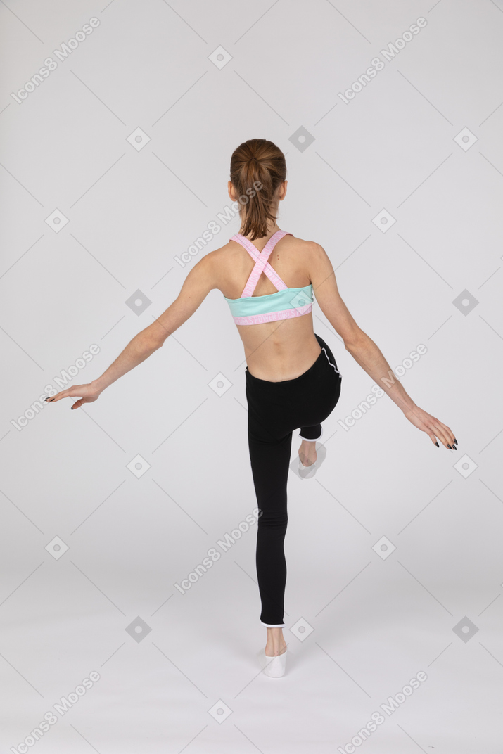 Vista traseira de uma adolescente em roupas esportivas estendendo as mãos e levantando a perna