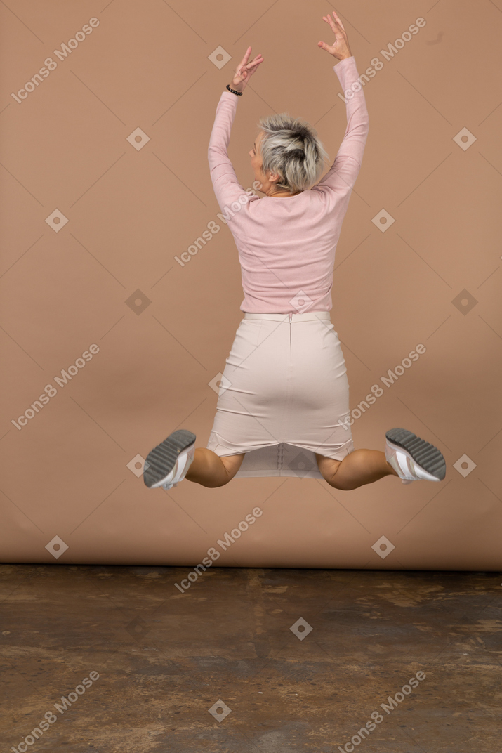Vista posteriore di una donna che salta con le braccia alzate