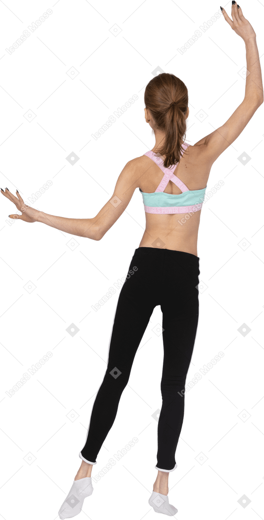 Back view of a teen girl in sportswear raising hands and putting her leg aside