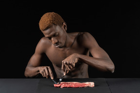 Front view of a young afro man cutting meat