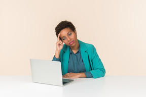 Nachdenklicher weiblicher büroangestellter, der vor laptop sitzt