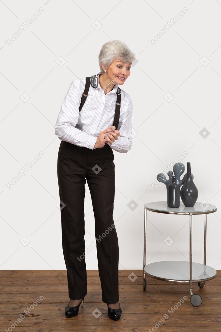 Front view of a pleased old l lady in office clothing holding hands together