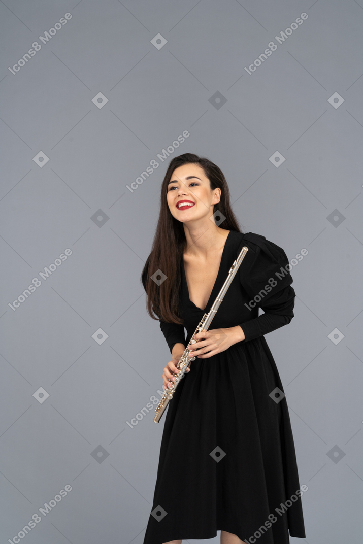 Vista frontal de uma jovem sorridente de vestido preto segurando uma flauta