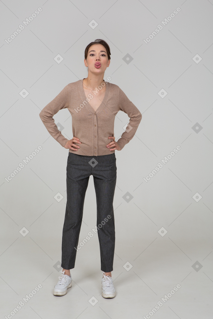 一位年轻的女士在套头衫和裤子po着嘴，把手放在臀部上的前视图