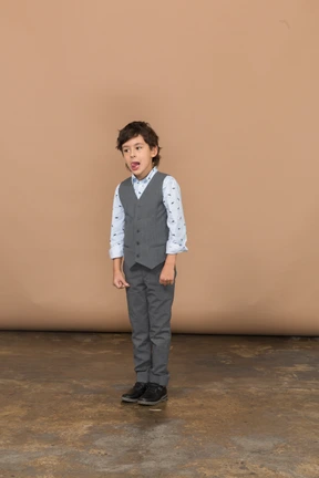 Front view of a cute boy in grey suit making faces and showing tongue