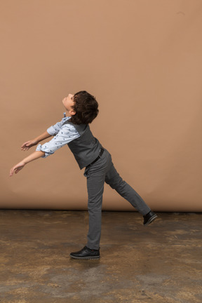 Vista laterale di un ragazzo in abito grigio in piedi su una gamba con le braccia estese