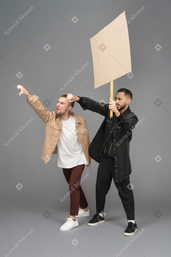 Vista di tre quarti di due giovani uomini con un cartellone pubblicitario rivolto da qualche parte in modo aggressivo