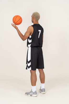 Three-quarter back view of a young male basketball player holding a ball