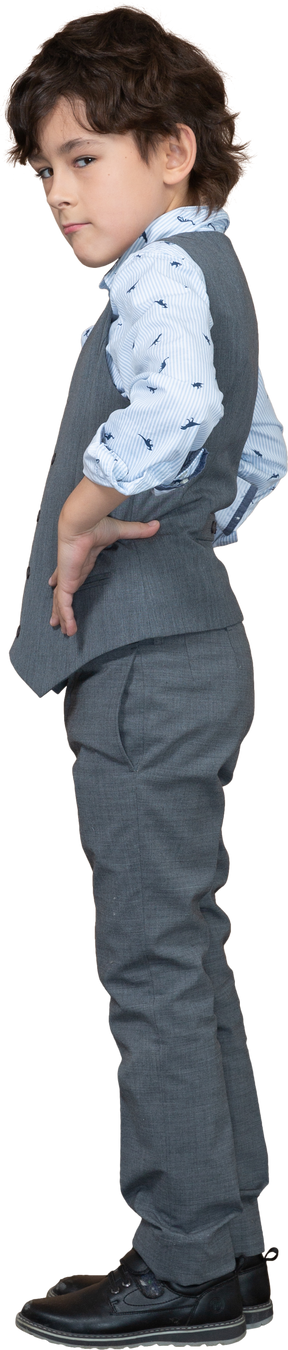 Vista laterale di un ragazzo carino in abito grigio in posa con le mani sui fianchi