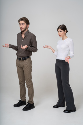 Vista di tre quarti di una giovane coppia interrogativa in abiti da ufficio