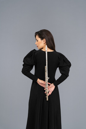 Вид сзади молодой леди в черном платье, держащей флейту позади