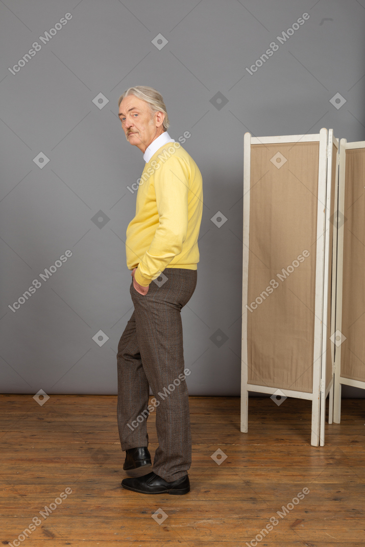 Vista laterale di un uomo anziano che mette la mano in tasca mentre guarda la fotocamera