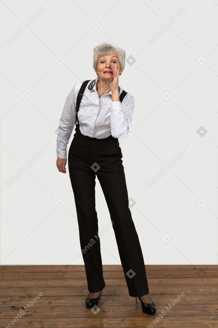 Vista frontal de uma mulher idosa com roupas de escritório, parada na sala e contando um segredo