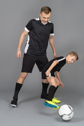 De cuerpo entero de un joven entrenando a un niño pequeño cómo jugar fooyball